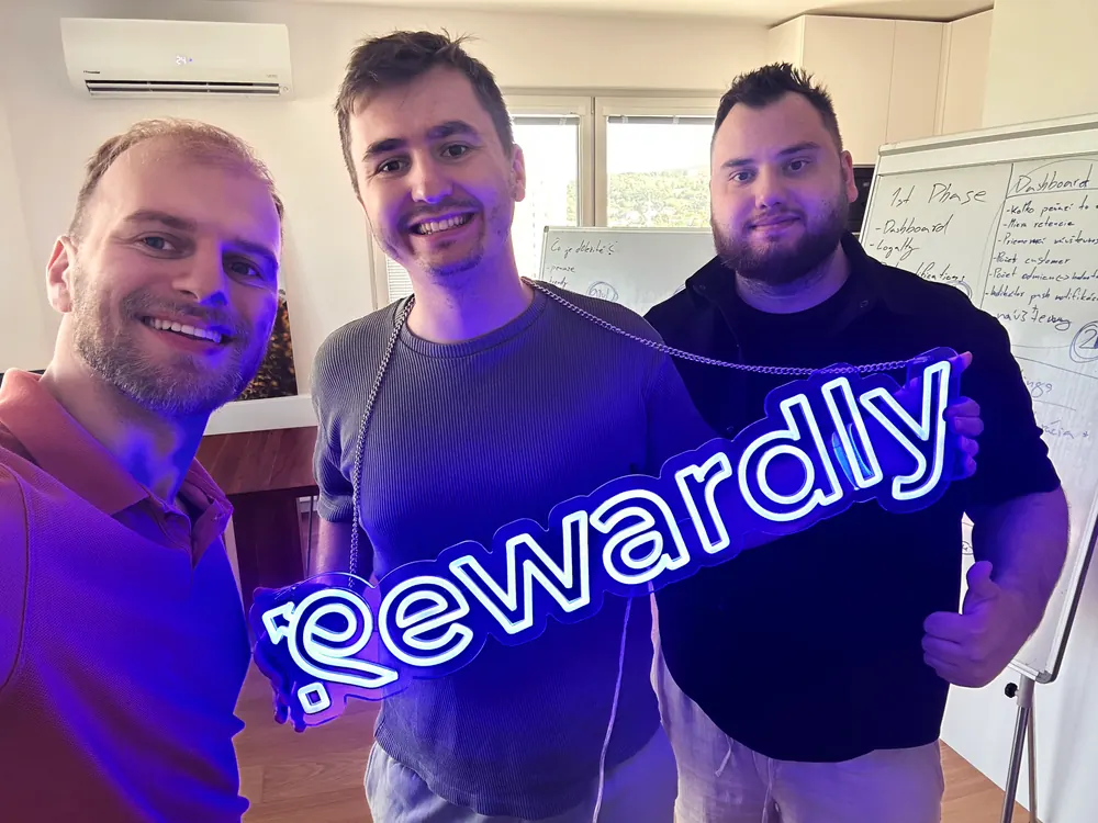 Three of the Rewardly team holding the neon Rewardly sign